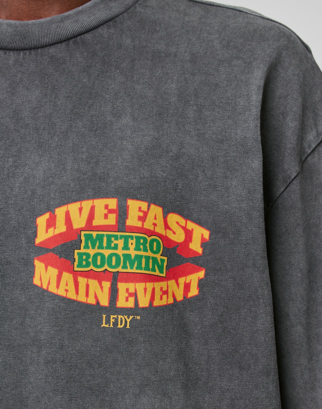 The LFDY Metro Boomin Tee by LIVE FAST DIE YOUNG is a gray oversized 100% Baumwolle shirt with bold yellow and red LIVE FAST MAIN EVENT, green/yellow METRO BOOMIN at the center, small yellow LFDY below, and a unique Ärmelprint.
