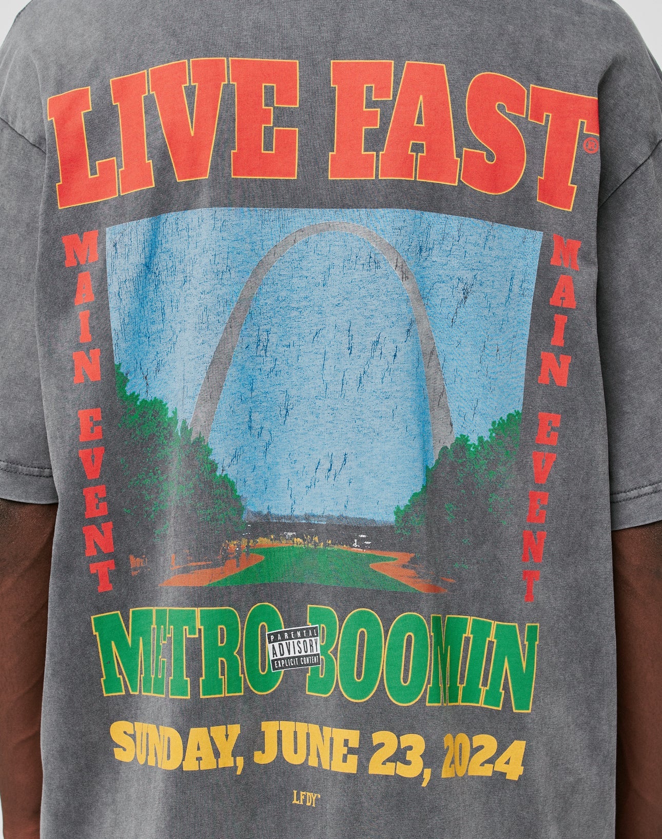 The LFDY Metro Boomin Tee by LIVE FAST DIE YOUNG is a gray 100% Baumwolle shirt featuring the Gateway Arch graphic, bold red and yellow event text, an Ärmelprint detail, and a parental advisory label.
