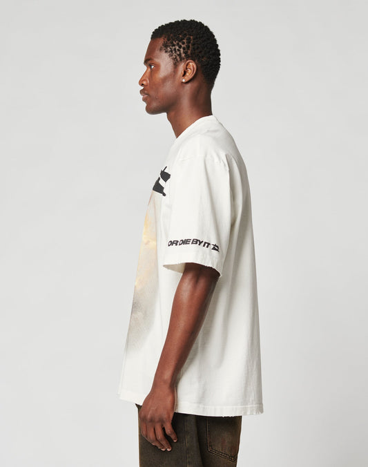 A man stands in profile against a plain background, wearing the LIVE FAST DIE YOUNG LFDY Angel Tee with front and sleeve print, paired with dark pants.