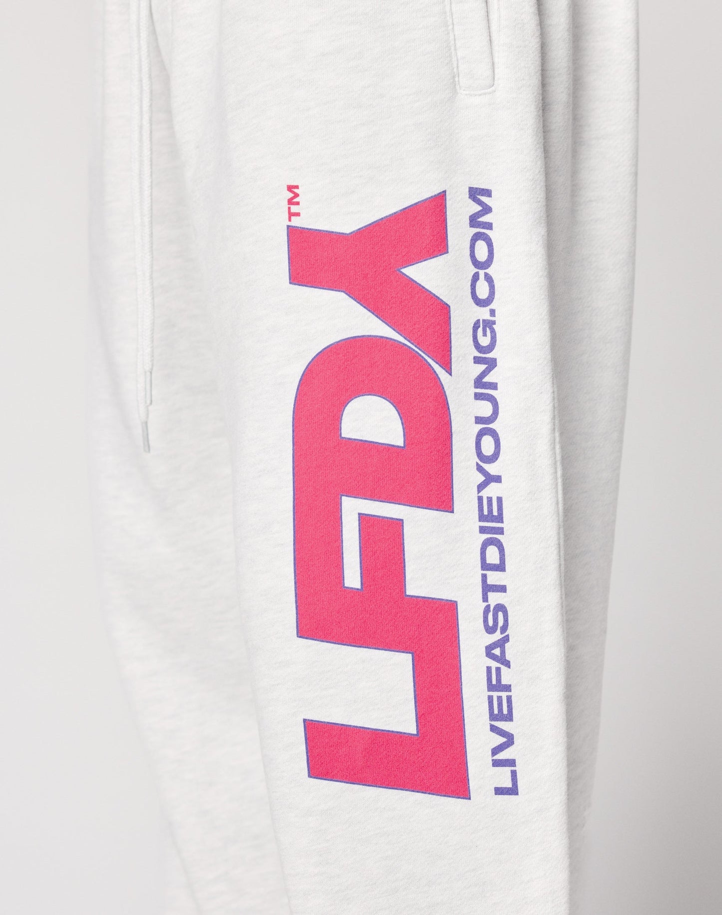 Close-up of the LIVE FAST DIE YOUNG LFDY Racing Wide Jogger in light gray, featuring a wide elastic waistband, bold pink and purple LFDY text, and “LIVEFASTDIEYOUNG.COM” printed vertically down the straight leg.
