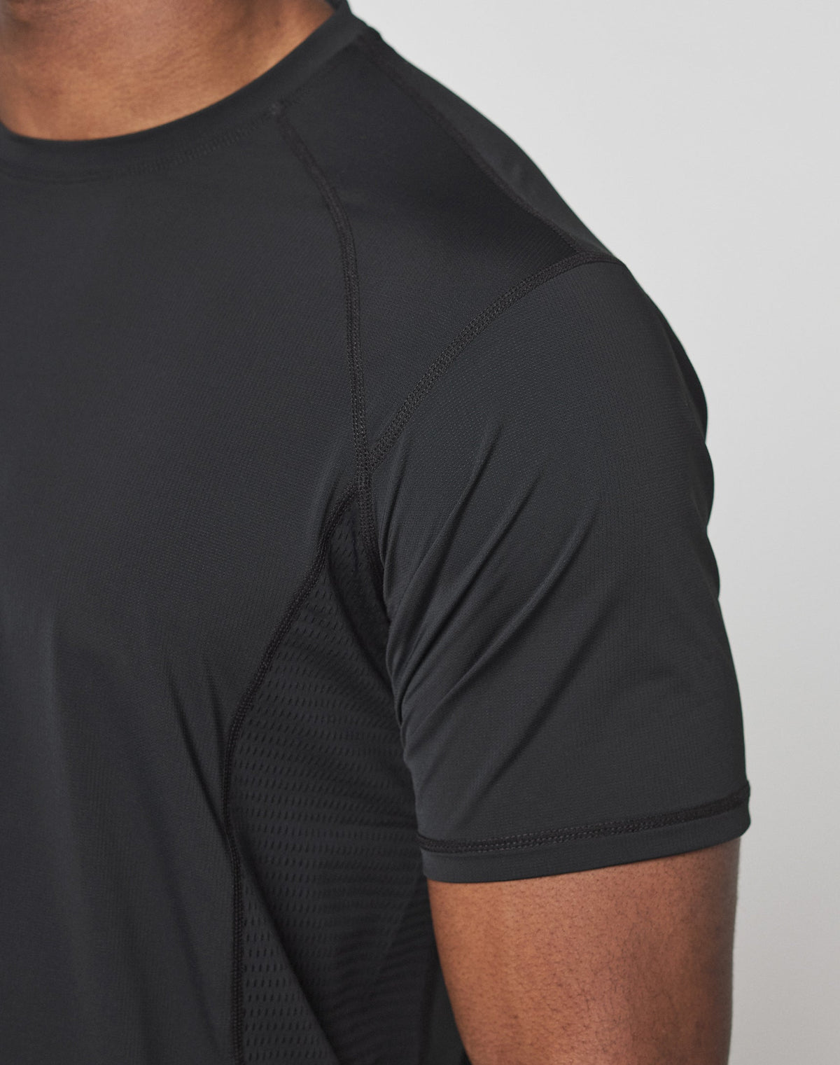 Close-up of a person wearing the LIVE FAST DIE YOUNG Live Fast Performance Tee, a fitted black short-sleeve athletic shirt made from stretchy Nylon Spandex. Only the upper torso and arm are visible against a plain light background.