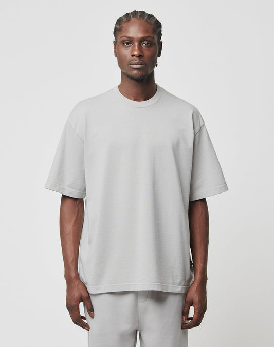 A person with braided hair faces forward, wearing an Oversize Fit Basic Heavy Tee by LIVE FAST DIE YOUNG in light gray and matching pants, both made from 100% Baumwolle, against a plain white background.