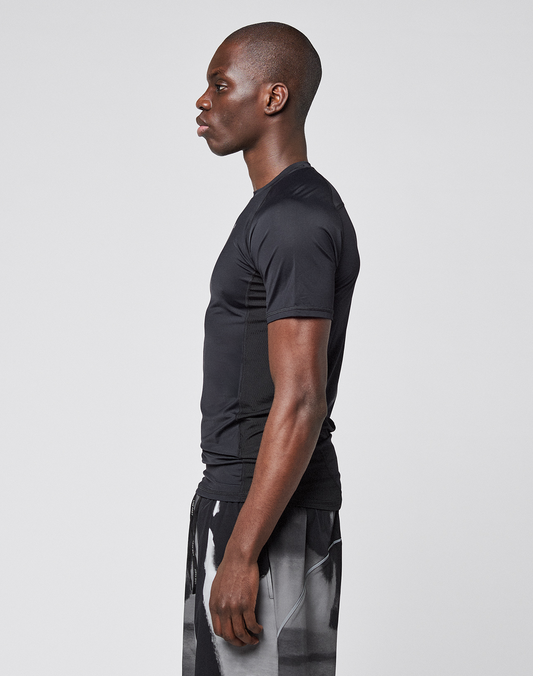 A man stands in profile facing left, wearing a LIVE FAST DIE YOUNG LFDY Performance Slim Tee and patterned shorts with leichtes Obermaterial, set against a plain light gray background.