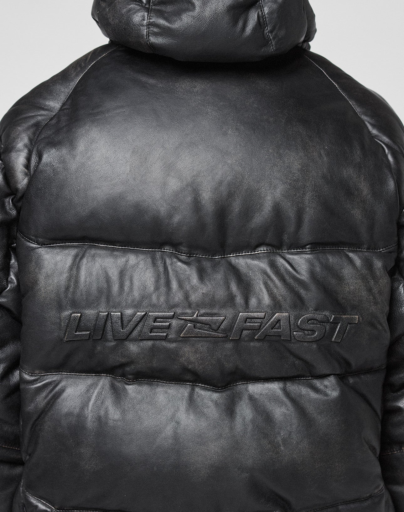 A close-up of the back of the black Live Fast Leather Puffer Jacket by LIVE FAST DIE YOUNG, featuring an oversize fit and an embossed Live Fast Logo across the upper back.