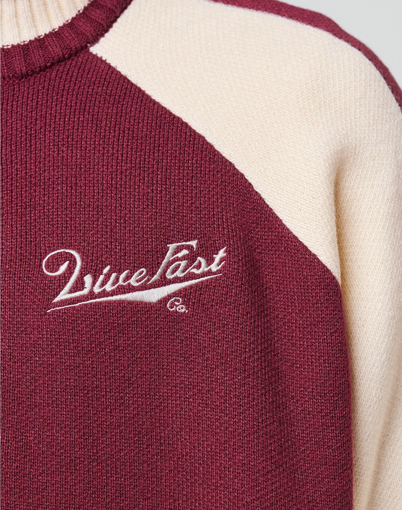 A young man with short curly hair and a neutral expression stands against a plain background, wearing the LIVE FAST DIE YOUNG Boxy Knit Zip Jacket in maroon and cream, featuring "MissList" on the chest, paired with light blue jeans.