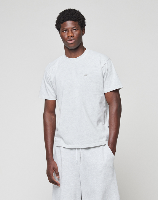 A man stands against a plain light background wearing a light gray LIVE FAST DIE YOUNG Basic Chest Tee with a small logo on the chest and matching shorts.