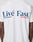 Back view of a person wearing the Live Fast Paris Tee by LIVE FAST DIE YOUNG, a white regular fit made from 100% Baumwolle, featuring bold Livé Fast™ blue text with red and blue underlines—a standout front and back design.