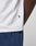 Close-up of a person wearing the LIVE FAST DIE YOUNG Live Fast Paris Tee in white with a small black tag on the hem, paired with blue pants featuring a visible zipper pocket. Plain background highlights the side torso and hip area.