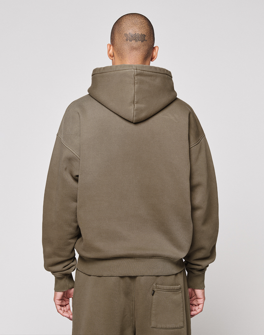 A person wearing the LIVE FAST DIE YOUNG Live Fast Rhinestone Hooded in olive green stands with their back to the camera, showcasing its oversized fit and a tattoo on their shaved head. Matching pants complete the vintage-inspired look.