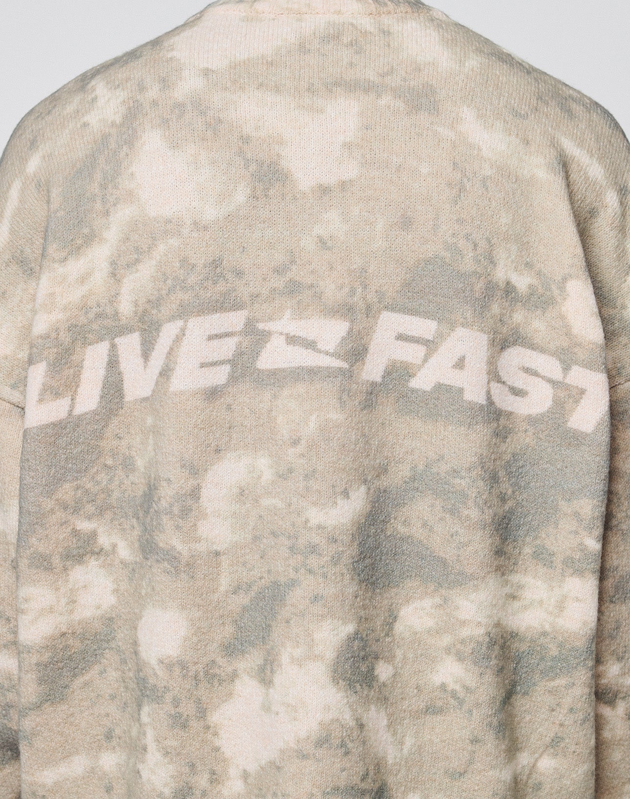 A close-up of the back of the Live Fast Boucle Sweater by LIVE FAST DIE YOUNG, featuring an oversize fit in beige and light brown tie-dye with "LIVE FAST" printed in bold white letters across the shoulders.