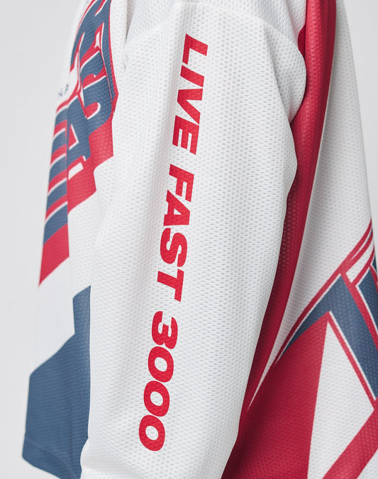 A close-up of the LFDY Racetrack Jersey by LIVE FAST DIE YOUNG shows a white, red, and blue sleeve with bold red LIVE FAST 3000 lettering. Made from 100% polyester, its dynamic look is enhanced by multi-logo prints.