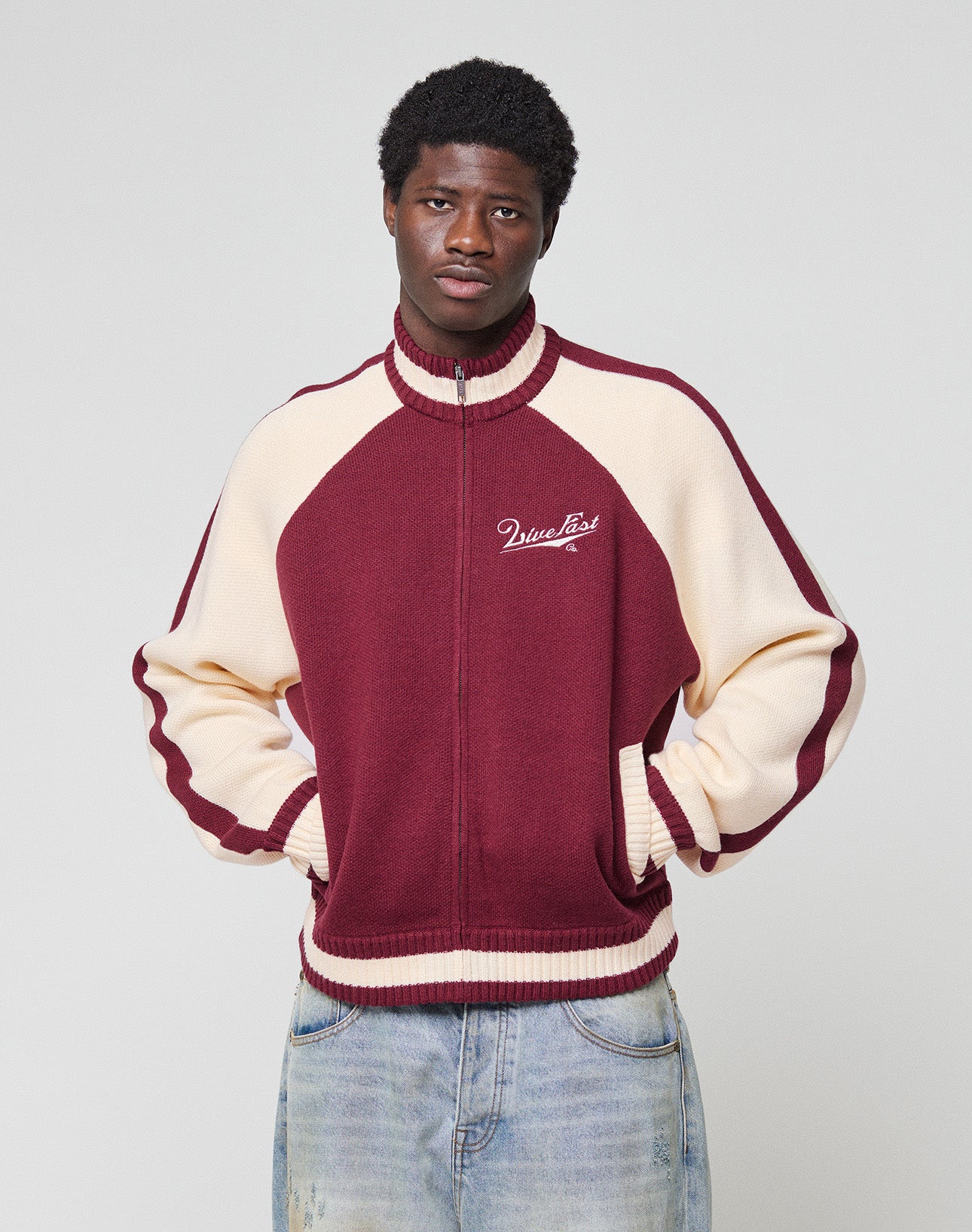 The back of the maroon and cream Boxy Knit Zip Jacket by LIVE FAST DIE YOUNG features intarsia-knit with a galloping horse graphic above bold, stylized “Live Fast Co.” text.