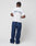 A person stands facing away, showcasing the LIVE FAST DIE YOUNG Live Fast Paris Tee, a regular fit white t-shirt with blue and red Live Fast front and back print, paired with loose navy pants and white shoes against a plain white background.
