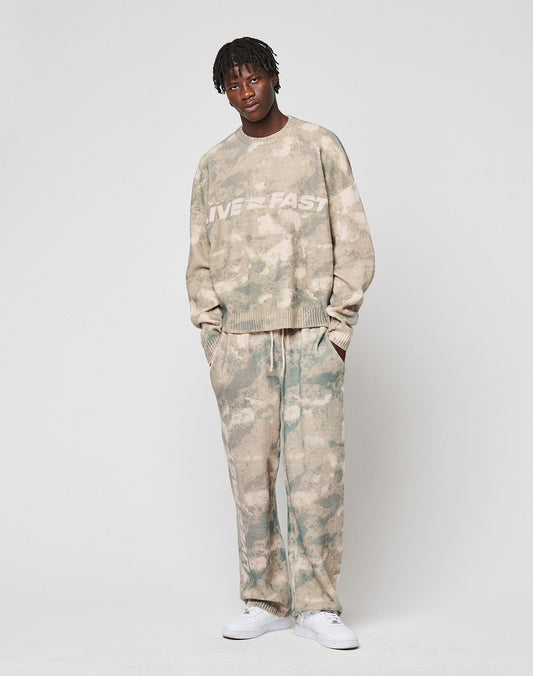 Wearing the LIVE FAST DIE YOUNG Live Fast Boucle Sweater in an oversize beige and green tie-dye fit, with matching pants and white sneakers. The set features the signature Live Fast Stick and is made from soft polyester.