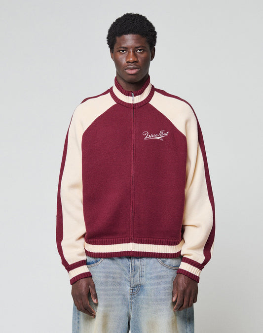 A young man with short curly hair and a neutral expression stands against a plain background, wearing the LIVE FAST DIE YOUNG Boxy Knit Zip Jacket in maroon and cream, featuring "MissList" on the chest, paired with light blue jeans.