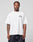 A man stands against a plain background, wearing the LIVE FAST DIE YOUNG Live Fast London Tee, an oversize fit 100% cotton white T-shirt with a front print, paired with dark baggy pants. He looks directly at the camera with a neutral expression.