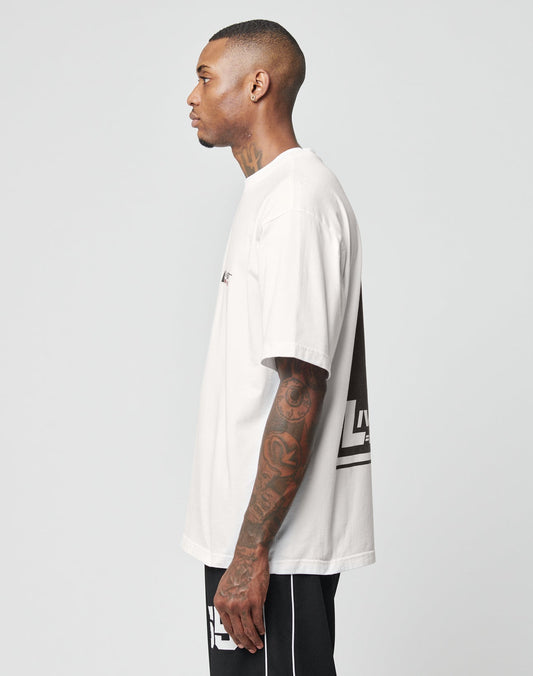 A man with tattoos on his neck and right arm stands in profile against a plain background, wearing the LFDY Industries Tee by LIVE FAST DIE YOUNG, featuring black front and back prints, paired with black shorts with white stripes.