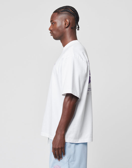 A man with braided hair stands in profile against a plain background, wearing a LIVE FAST DIE YOUNG Basic 280 Tee and light blue shorts.