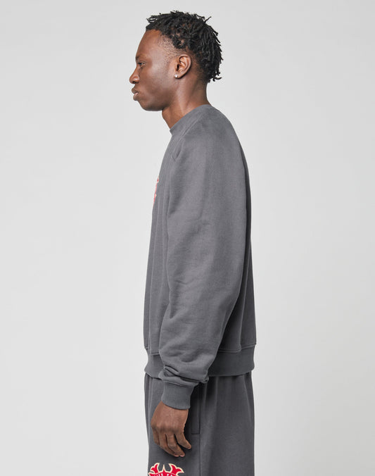 A person stands in profile against a light gray background, wearing the LIVE FAST DIE YOUNG DY Sweater in an oversized dark gray fit with raglan sleeves, paired with matching shorts featuring red and white graphic details.