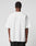 A person stands with their back to the camera, wearing the LIVE FAST DIE YOUNG Fuck Die Young Tee—a plain white 100% Baumwolle short-sleeve t-shirt—and black pants against a neutral light background.