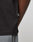 Close-up of the side of a black Live Fast Plain Tee by LIVE FAST DIE YOUNG, showing a small fabric tag. The tee is worn by a person with dark skin and gray pants visible at the bottom edge.