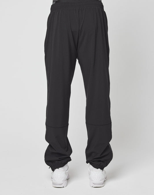 A person wearing LIVE FAST DIE YOUNG Live Fast Performance Running Pants in an oversize fit with an elastic waistband and white sneakers stands against a plain background, with the image focused on the back of the pants.