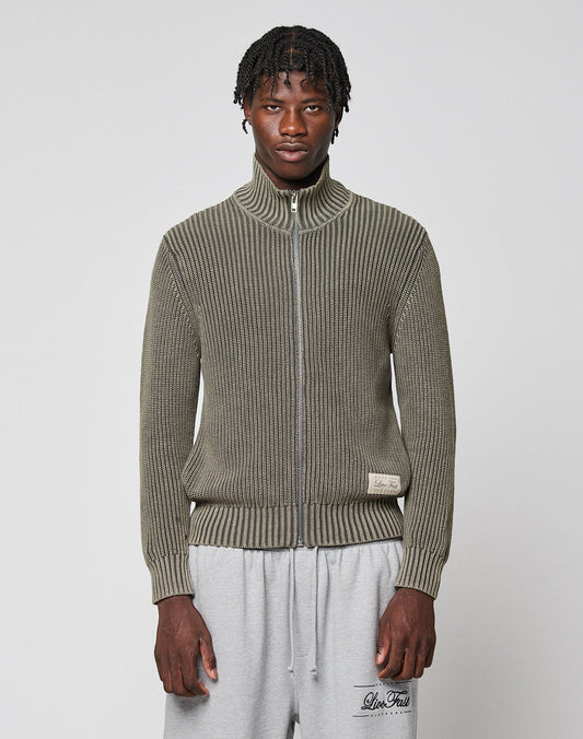A man with short twisted hair wears the LFDY Knit Jacket from LIVE FAST DIE YOUNG in olive green and light gray sweatpants, standing against a plain white background. | model