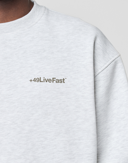 A close-up of the Basic +49 Chest Sweater by LIVE FAST DIE YOUNG in light gray Oversize Fit, showing only the upper torso and the +49LiveFast™ print on the left chest.