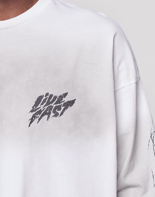 Close-up of the LFDY Logo Longsleeve by LIVE FAST DIE YOUNG, a white shirt with vintage effect, featuring a faded gray patch and bold, distressed "LIVE FAST" text. Part of the wearer’s neck and shoulder is visible.