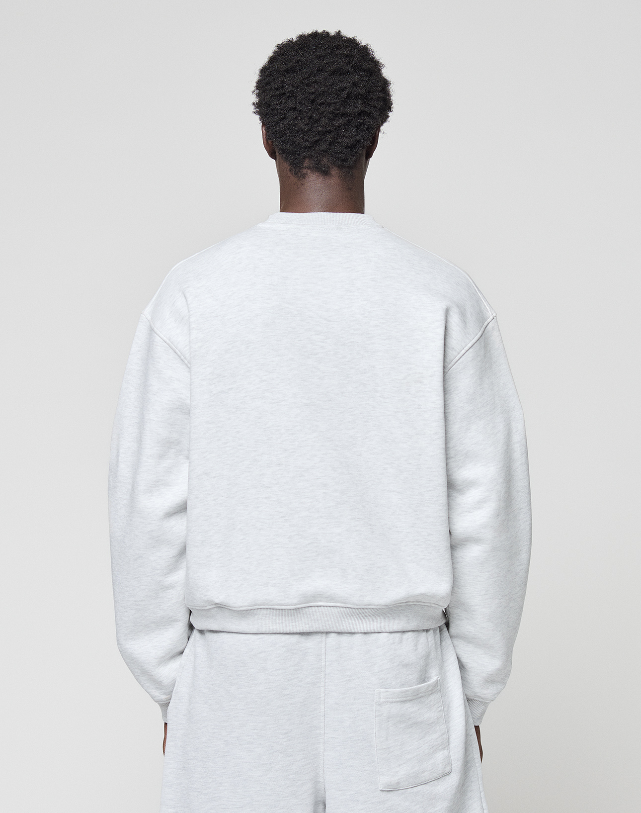 A person is seen from behind wearing the LIVE FAST DIE YOUNG Basic +49 Chest Sweater in an oversize fit, light gray shade, paired with matching shorts, standing against a plain light background.
