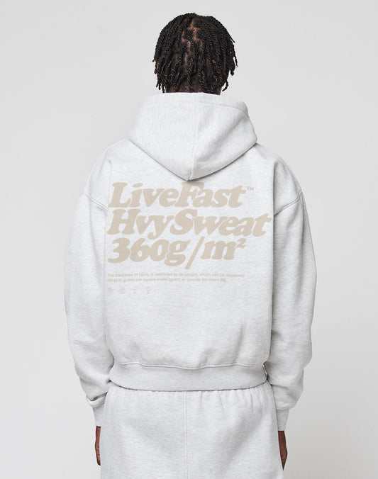 A person with braided hair is seen from the back wearing an oversize fit light gray Basic 360 Hooded and sweatpants by LIVE FAST DIE YOUNG, featuring a bold beige “Live Fast Hyv Sweat 360g/m²” backprint.