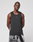 A man stands against a plain light background wearing the LIVE FAST DIE YOUNG LFDY Performance Tank, featuring leichtes Obermaterial, and black-and-white patterned shorts. His arms are relaxed behind his back with a neutral expression.