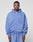 A man wears the LIVE FAST DIE YOUNG Basic Hooded Zip in light blue with Kapuze, front pockets, and handgefertigtem Fade-Effekt, standing before a plain light gray background and looking neutrally at the camera.