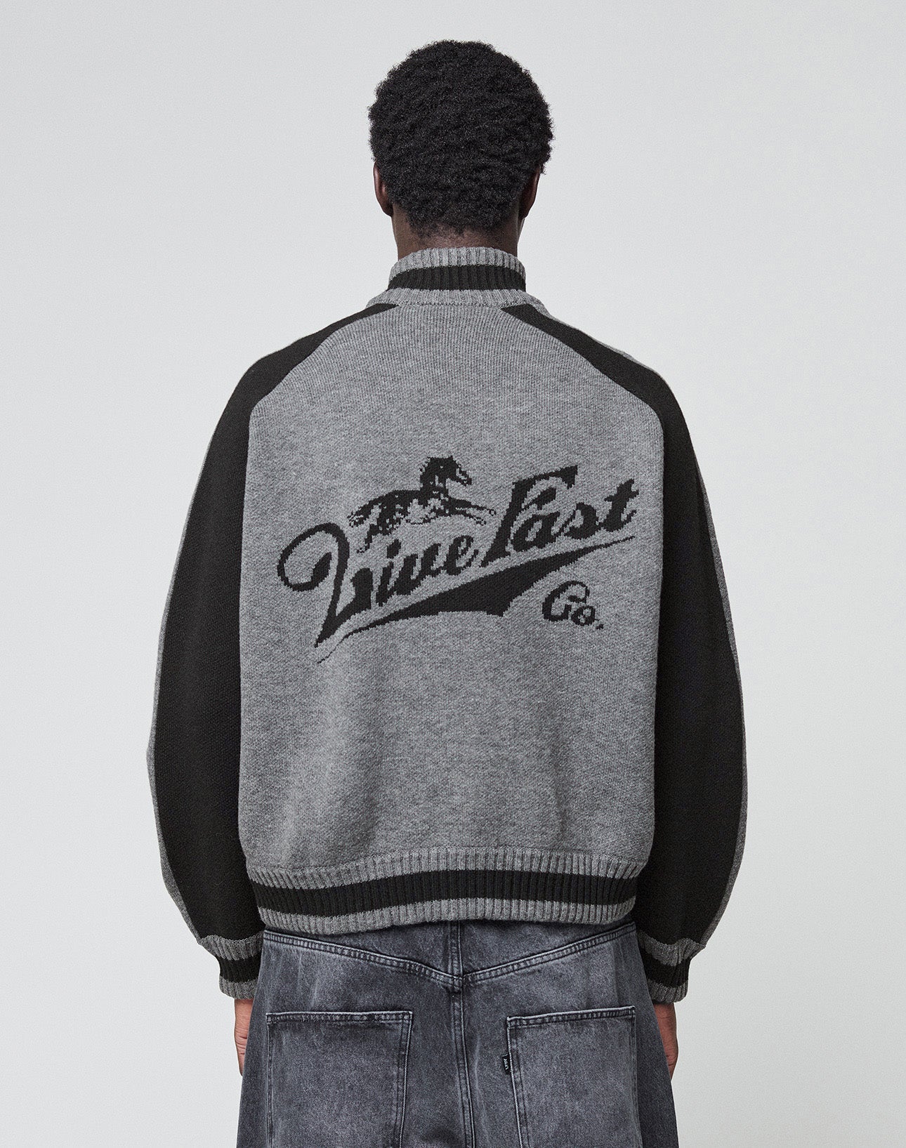 The Boxy Knit Zip Jacket by LIVE FAST DIE YOUNG features gray and black intarsia-knit with dark raglan sleeves, a running horse graphic, “Live Fast Co.” on the back, and ribbed cuffs, hem, and collar for an oversize fit.| plain
