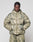 A person with cornrow braids wears the LIVE FAST DIE YOUNG Live Fast Puffer Jacket in green and beige camouflage with reflective print and matching oversized pants, standing against a plain light gray background.