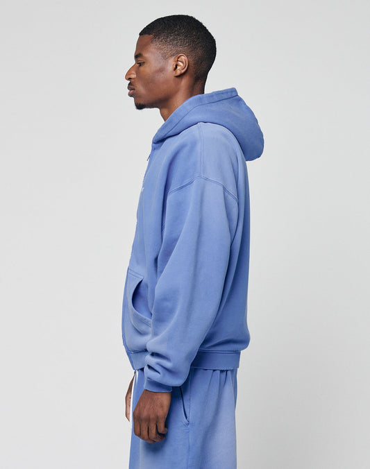 A man in profile wears a matching light blue LIVE FAST DIE YOUNG Basic Hooded Zip and sweatpants with handcrafted fade effect, facing left against a plain light gray background.