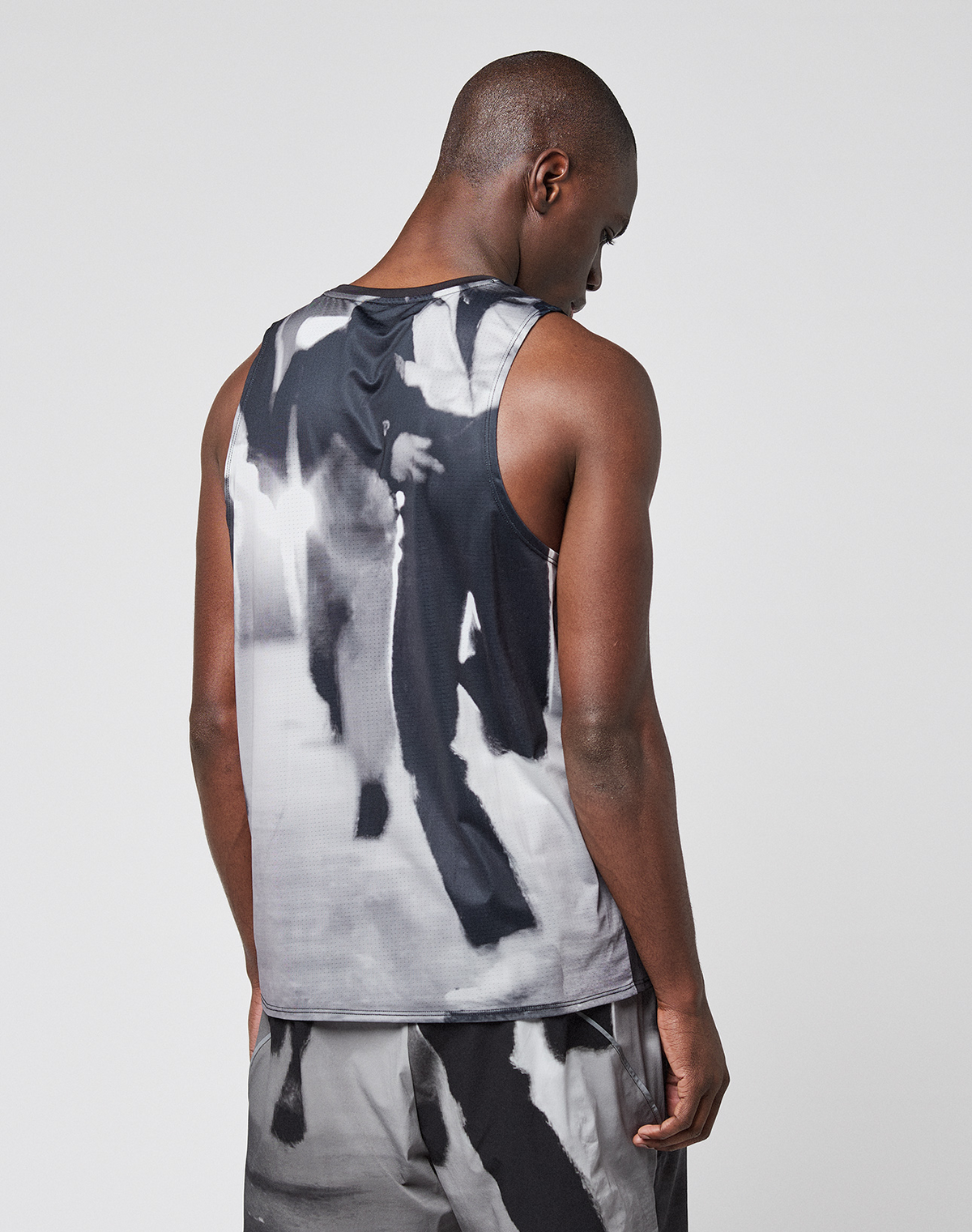 A person stands facing away from the camera, wearing a LIVE FAST DIE YOUNG LFDY Performance Tank and shorts with a black, white, and gray abstract pattern against a plain light background.