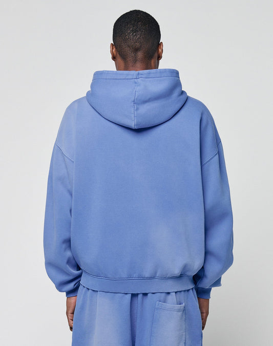 A person wearing a loose-fitting, light blue LIVE FAST DIE YOUNG Basic Hooded Zip sweatshirt and matching sweatpants stands facing away, highlighting the handcrafted fade effect against a plain light background.