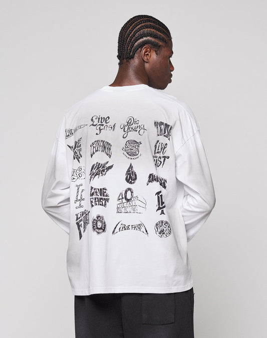 A person with braided hair wears the LFDY Logo Longsleeve by LIVE FAST DIE YOUNG, a white oversized 100% Baumwolle shirt with black graphic designs and text on the back, standing against a plain light gray background.