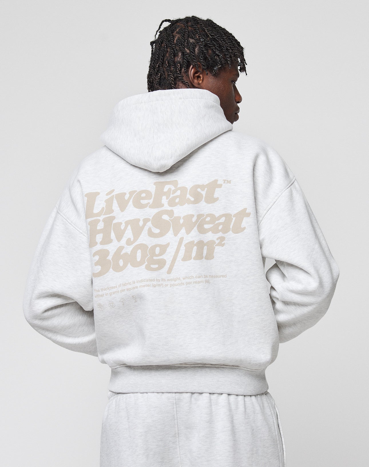 Someone wears the LIVE FAST DIE YOUNG Basic 360 Hooded in light gray with the hood up, showing bold beige “Live Fast Hvy Sweat 360g/m²” text on the back, paired with matching gray sweatpants for a full cotton look.