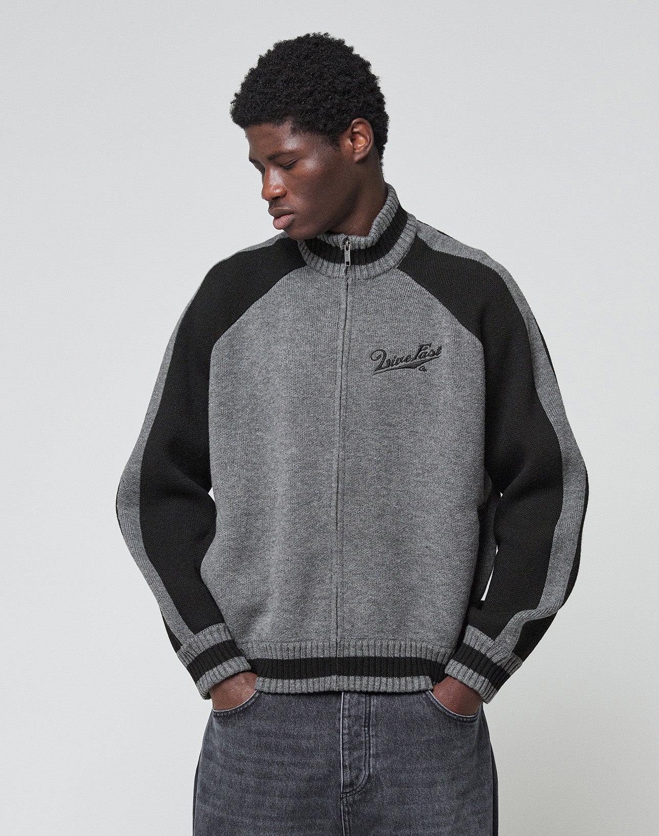 A close-up of the back of the Boxy Knit Zip Jacket by LIVE FAST DIE YOUNG, featuring an oversized gray fit with black "Live Fast Co." text and an intarsia-knit running horse above.