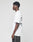A young man with short curly hair stands in profile against a plain background, wearing the LIVE FAST DIE YOUNG LFDY Sharkhunter Tee—an oversized white t-shirt made from 100% Baumwolle with black text on the back—and dark pants.