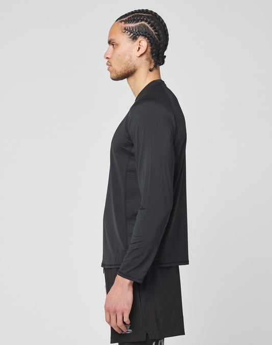 A man with braided hair stands in profile, wearing the LIVE FAST DIE YOUNG Live Fast Performance Longsleeve in slim fit and black shorts with a mesh insert, set against a plain light gray background.