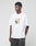 A young man wears the LIVE FAST DIE YOUNG LFDY Sharkhunter Tee—an oversize white t-shirt with a colorful graphic—standing against a plain background, gazing to the side with his hands in his dark pants pockets.