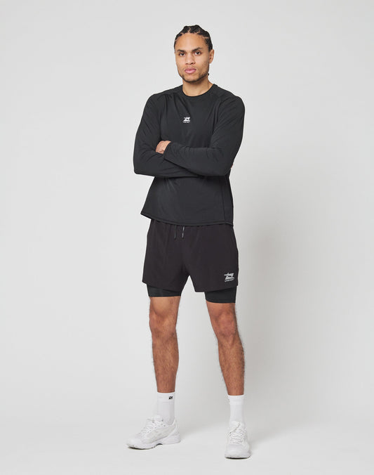 A man stands against a white background wearing the LIVE FAST DIE YOUNG Live Fast Performance Longsleeve, paired with black shorts, white socks, and white sneakers. His arms are crossed as he looks slightly to the side.