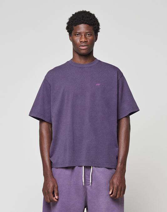 A man stands against a plain light background wearing the LIVE FAST DIE YOUNG Basic Evidence Tee in purple and matching drawstring shorts made from 100% Baumwolle, looking straight at the camera with a neutral expression.