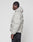 A person with braided hair wears the LIVE FAST DIE YOUNG Live Fast Puffer Jacket in light gray with an oversize fit, hood, reflektierender Print, and subtle sleeve and side graphics, standing in profile against a plain white background.
