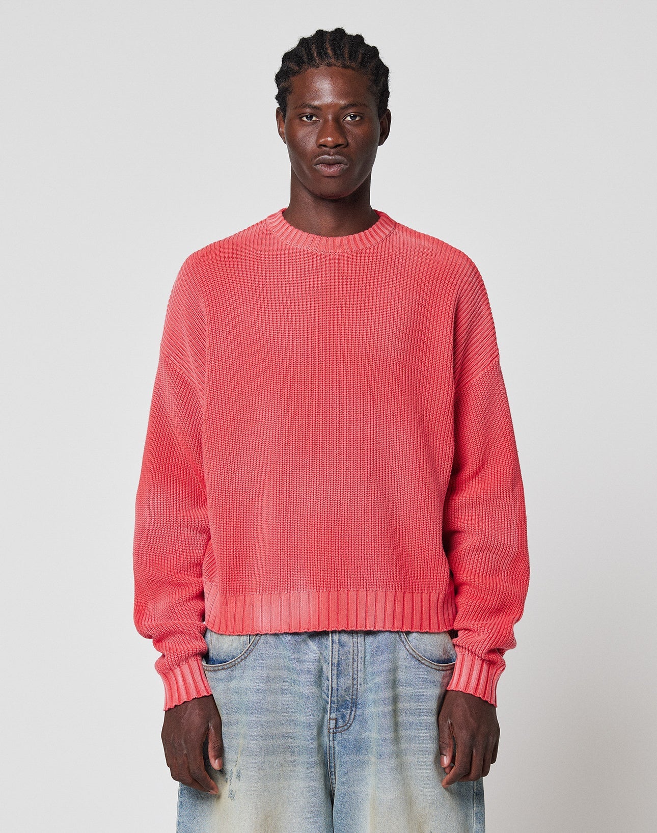 A person with braided hair wears the LFDY Washed Knit Sweater by LIVE FAST DIE YOUNG and faded light blue jeans, standing against a plain white background.