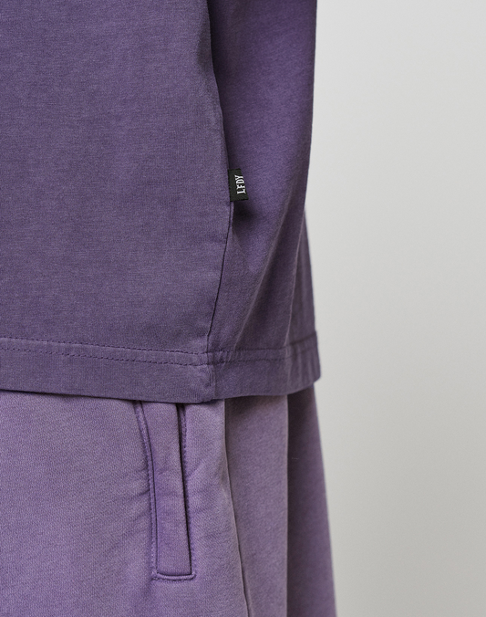 Close-up of a person wearing the LIVE FAST DIE YOUNG Basic Evidence Tee in purple with matching pants, highlighting the side seam, waistband, and small black label. Crafted from 100% Baumwolle for comfort against a plain light background.