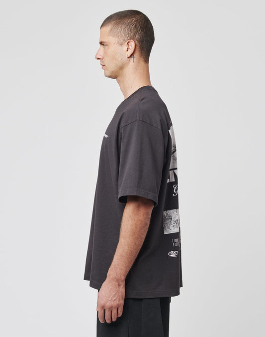 A man with short hair, wearing a loose-fitting LIVE FAST DIE YOUNG LFDY Cinema Tee and black pants, stands in profile against a plain white background.